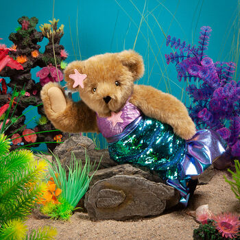 15" Mermaid Bear - Front view of standing jointed bear dressed in a blue sequin tail and purple top with shell embroidery an pink starfish applique and earpiece in an underwater scene - honey brown fur